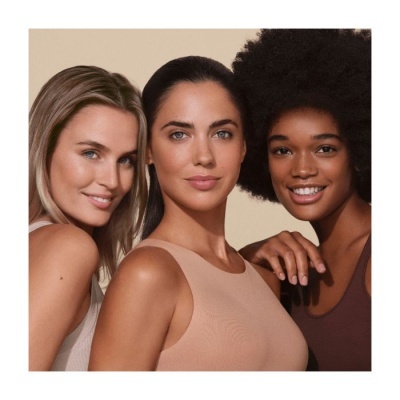 Três mulheres com tops sem mangas em cores neutras, fundo bege claro.