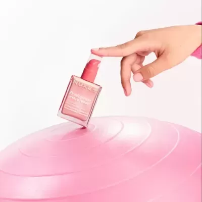Frasco rosa NUXE Prodigieuse Hyalu Boost sobre bola de exercício rosa