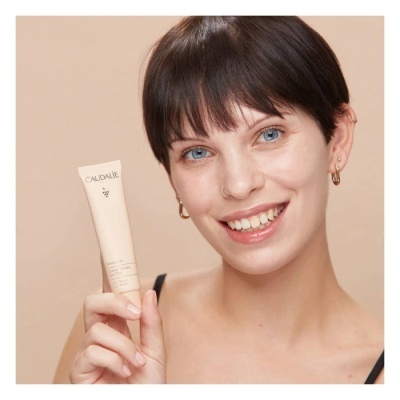 Mulher sorridente segurando tubo de produto CAUDALIE