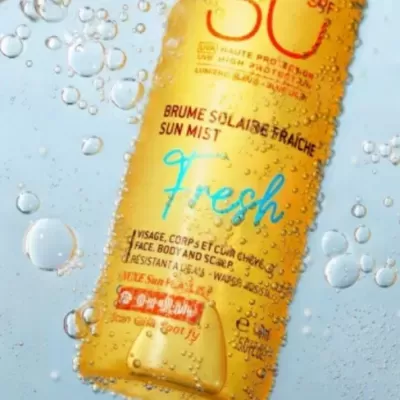 Frasco amarelo de spray de proteção solar com água ao redor, texto em francês e inglês