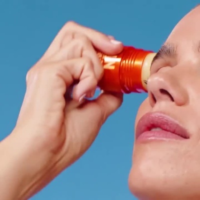 Frasco de sérum solar SPF 50 com stick sendo aplicado no rosto