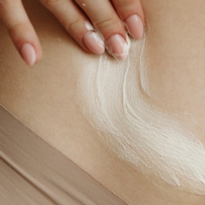 Pessoa aplicando creme branco na zona abdominal com cuecas bege