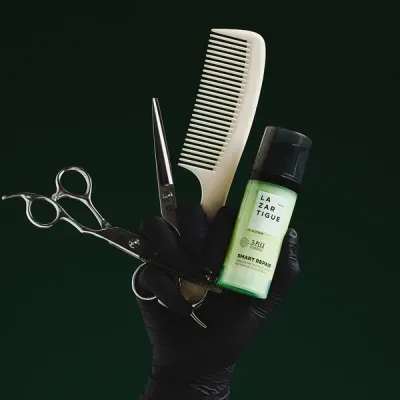 Mão com luva preta segurando tesouras, pente branco e frasco de cosmético verde