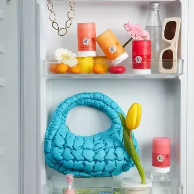 Frigorífico aberto com mala azul, vaso com tulipa amarela, latas THE BODY SHOP, óculos de sol e colar dourado.