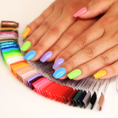 Mãos com unhas coloridas segurando paleta de amostras de vernizes de unhas