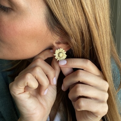 Brinco dourado em forma de girassol num ouvido