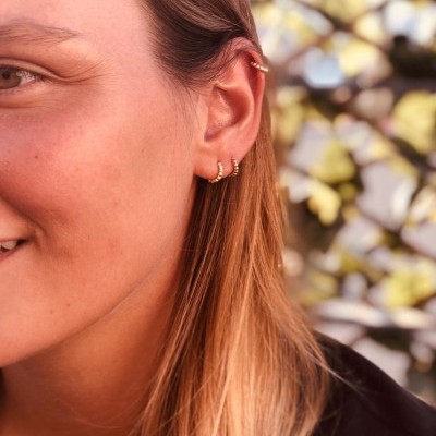 Mulher com brincos dourados em orelha esquerda e fundo natural desfocado