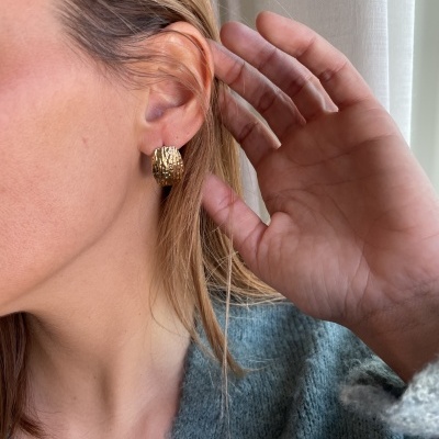 Brinco dourado texturizado em orelha de pessoa com cabelo loiro