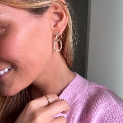 Brincos de argolas douradas e prateadas com anéis dourados em mulher de suéter rosa