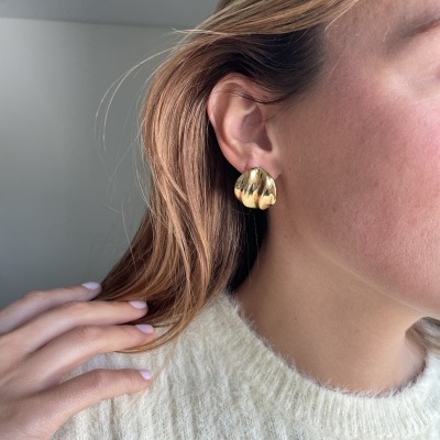 Brinco dourado ondulado usado por mulher com camisola branca