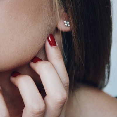 Mulher com brinco prateado em forma de flor e unhas vermelhas