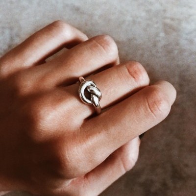 Anel de prata com nó usado na mão sobre fundo cinzento