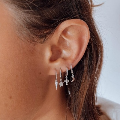 Quatro brincos pequenos em prata em orelha de mulher com cabelo castanho curto