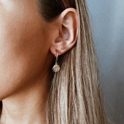 Orelha com dois brincos dourados, um pequeno e um com pendente redondo gravado