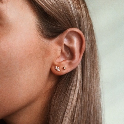 Brincos dourados pequenos numa orelha feminina com cabelo castanho claro.