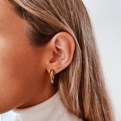 Orelha com brincos dourados e cabelo loiro.