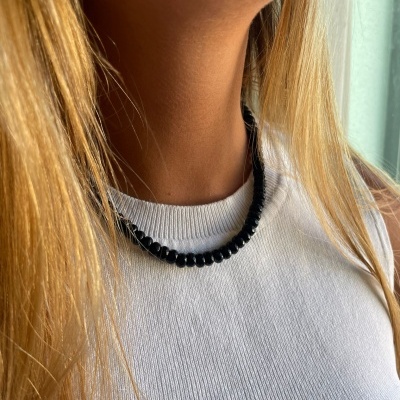 Colar de contas pretas usado em pescoço feminino com blusa branca e cabelo loiro
