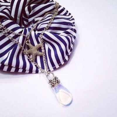 Colar com corrente prateada e pingente estrela do mar com gota transparente sobre pano riscado azul e branco.