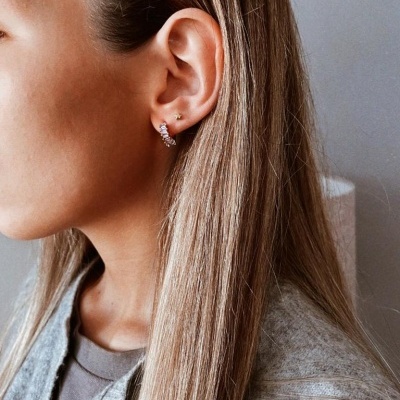 Mulher com brincos pequenos, cabelo loiro e suéter cinzento