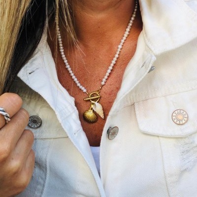Colar de pérolas com pendentes de concha e camisa branca com botões metálicos