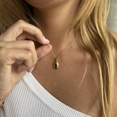 Colar pendente dourado oval com corrente fina no pescoço de mulher com top branco