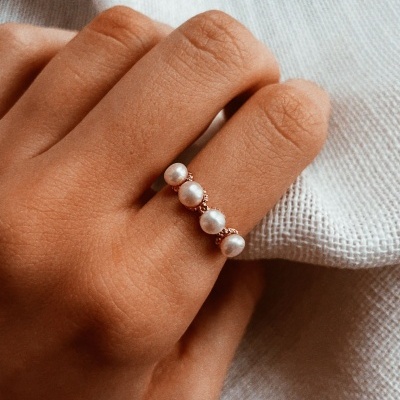 Anel com quatro pérolas brancas numa mão sobre tecido branco