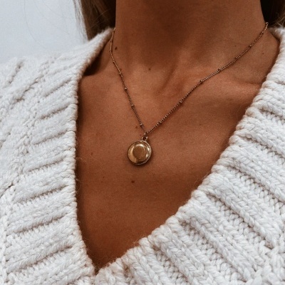 Colar dourado com pendente circular em suéter branco de malha grossa