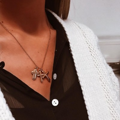 Colar dourado com três cruzes em mulher com blusa preta e casaco branco