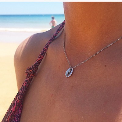 Colar prateado com pendente de búzio em pele bronzeada, fundo praia e mar azul