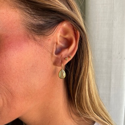 Orelha feminina com três brincos dourados, incluindo uma gota pendente.