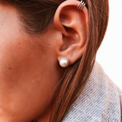 Ouvido feminino com brinco de pérola e brinco de argolas prateadas na cartilagem