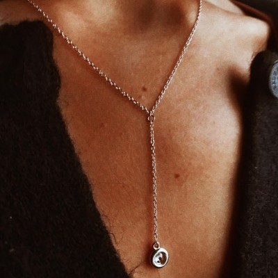 Colar prateado com pendente circular em pescoço de pessoa com casaco castanho escuro