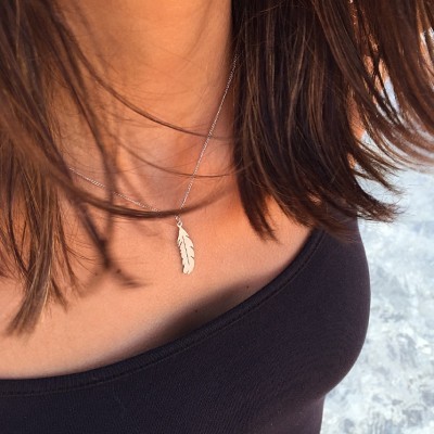 Colar prateado com pendente em forma de pena e pessoa com blusa preta