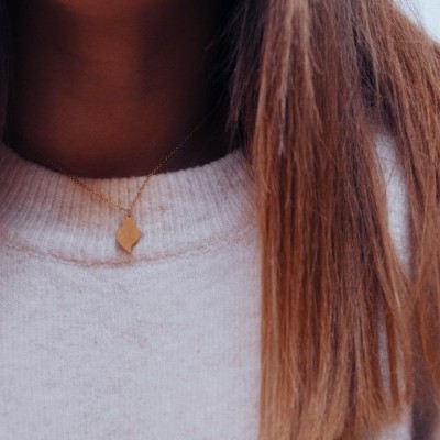 Colar dourado com pendente abstrato em pessoa com camisola cinza e cabelo castanho