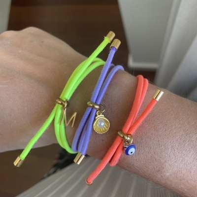 Pulseiras neon verde, lilás e laranja com pendentes dourados no pulso