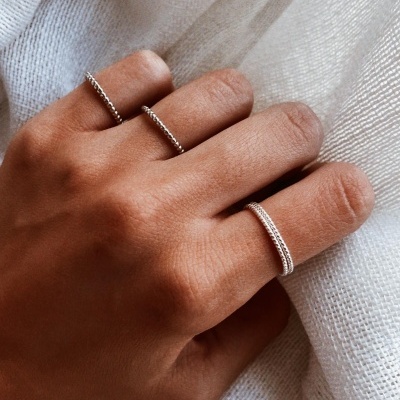 Mão com três anéis prateados finos e texturizados sobre tecido branco.