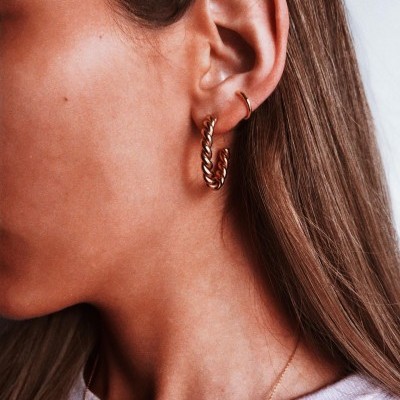 Brincos dourados em forma de argola com textura de corda no ouvido esquerdo