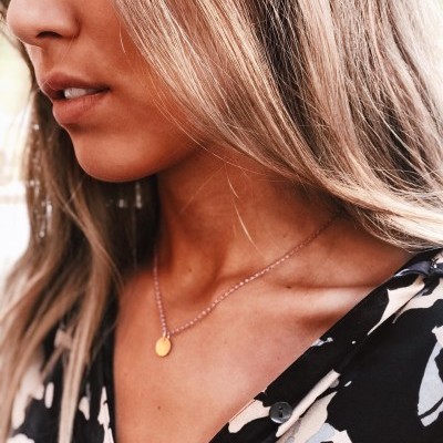 Mulher com colar dourado e blusa preta com padrões brancos e cinzentos