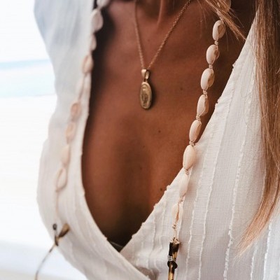 colar comprido com contas bege claro e detalhes em madeira, roupa branca com decote V e colar dourado com pendente oval