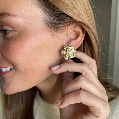 Brincos florais dourados com pérola no centro na orelha esquerda de mulher