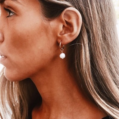 Brinco de argola dourado com pendente de pérola branca numa orelha feminina