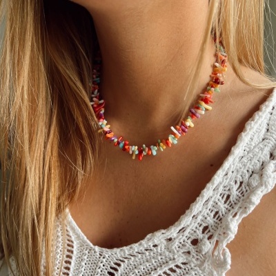 Colar de pedras coloridas em pescoço de mulher com camisola branca de malha