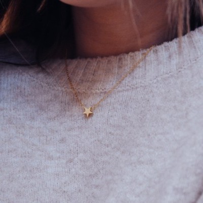 Colar dourado com pendente de estrela numa camisola bege claro