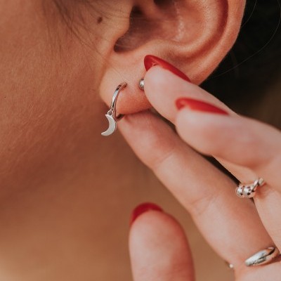 orelha com brincos prateados e unhas vermelhas