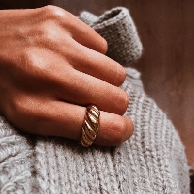 Anel dourado grosso em dedo com camisola cinzenta de malha