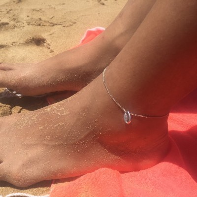 Tornozeleira prateada com concha num pé com areia na praia