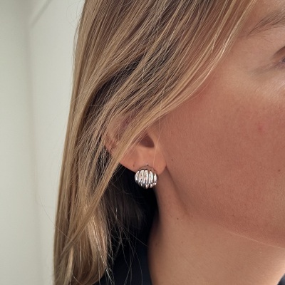 Brincos prateados ondulados em orelha feminina com cabelo loiro