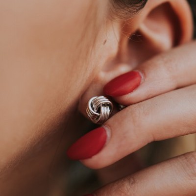 Brincos prateados entrelaçados na orelha com unhas vermelhas