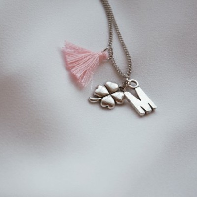 Colar com trevo e pendente letra M sobre tecido branco