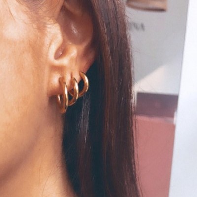 Três brincos de argola dourados na orelha de uma pessoa com cabelo castanho